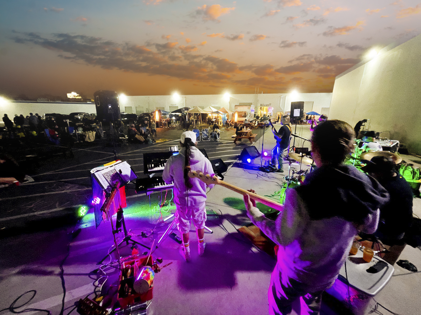 A live band playing at sunset with the Convoy Nights market and its vendor tents behind them, outside Kilowatt Brewing Kearny Mesa