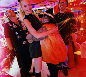 Friends in costume, cat ears, a witch hat and a jack-o'-lantern, under the BrewDoodle market tent at Kilowatt Ocean Beach.